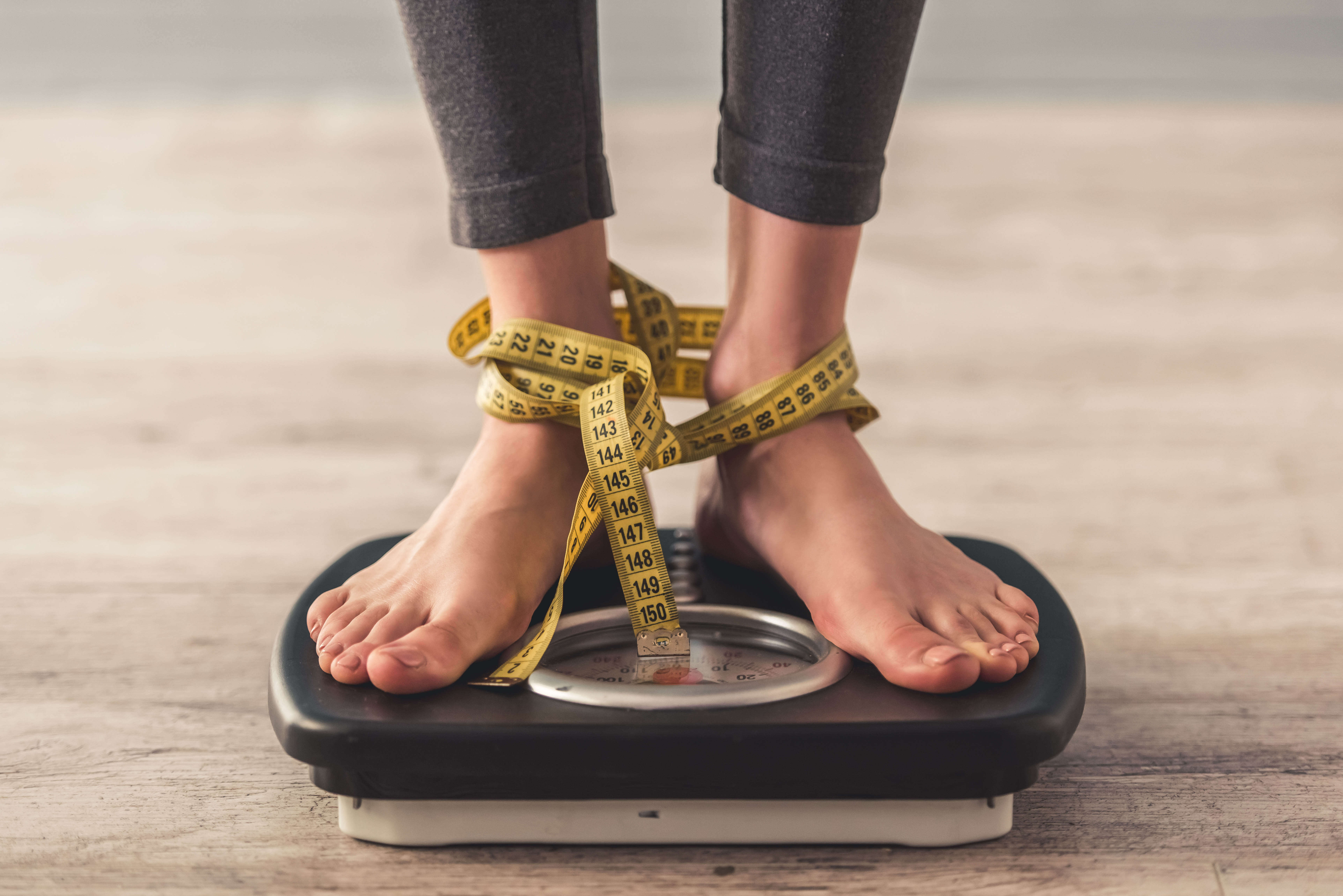 Close-up of feet standing on a scale with a measuring tape wrapped around their feet